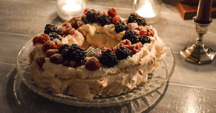 Whipped cream being spread across a crisp meringue shell